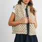 Woman wearing a patterned vest over a white shirt with a navy skirt on a plain background